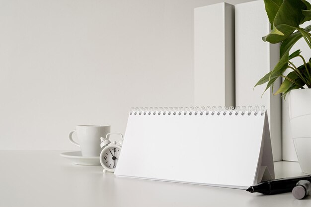 Machen Sie einen leeren spiralförmigen Kalender mit umkehrenden Blättern auf einem weißen Tisch mit Kaffeebüchern und Uhr
