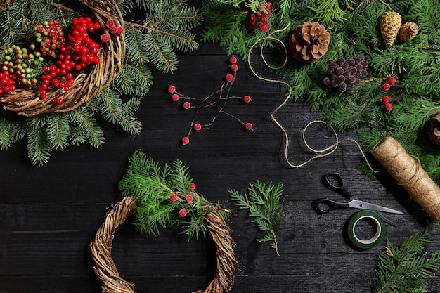 Machen Sie einen Weihnachtskranz mit Ihren eigenen Händen Fichtenzweig Weihnachtskranz und Geschenke auf einem schwarzen Holz...