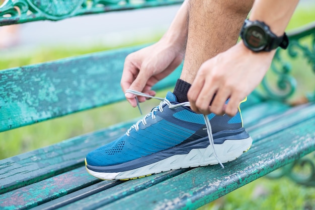 Macho adulto joven en ropa deportiva y smartwatch atar cordones de los zapatos en el parque