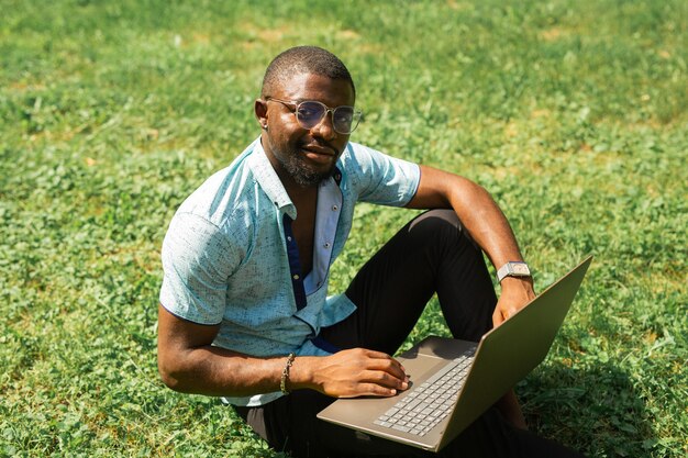 Macho africano de trabajo con ordenador portátil sobre la hierba en verano