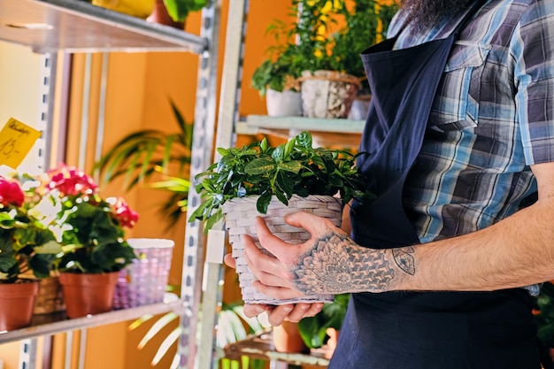 Macho barbudo com braços tatuados detém um pote com flores.