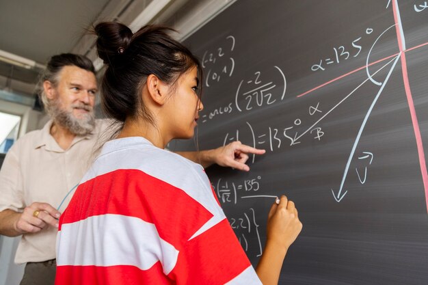 Macho caucásico maduro profesor de matemáticas de la escuela secundaria explica el ejercicio de pizarra para la educación del estudiante