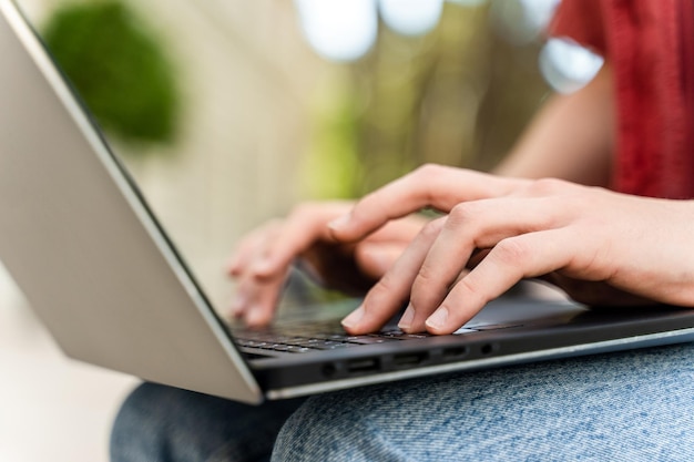 Macho digitando com a mão no laptop enquanto está sentado no banco na rua