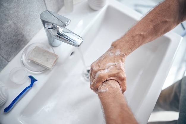 macho enjabonándose el dorso de la mano sobre el lavabo