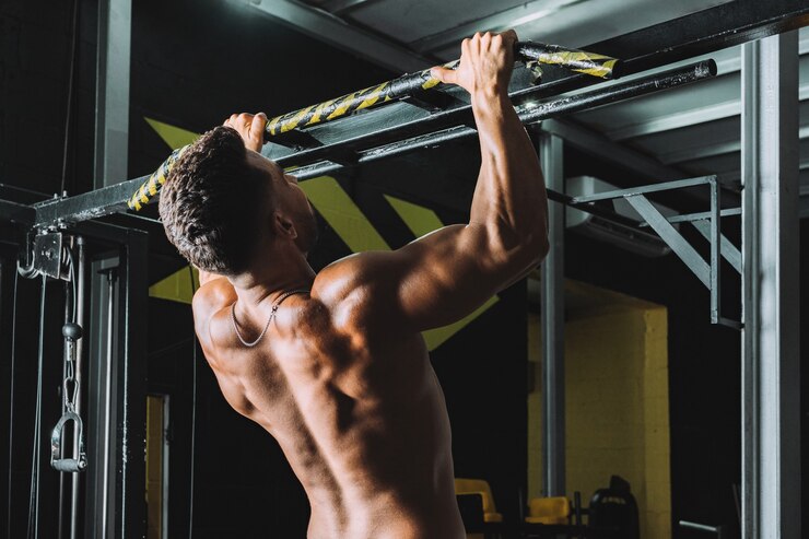 Macho fuerte haciendo dominadas en una barra en un gimnasio
