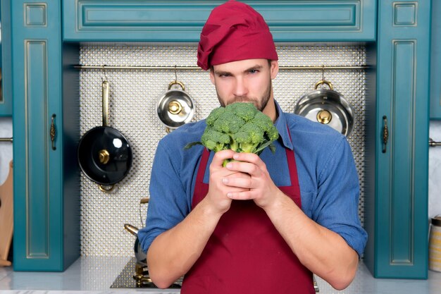 Macho in roter Kochmützenschürze halten grünen Brokkoli
