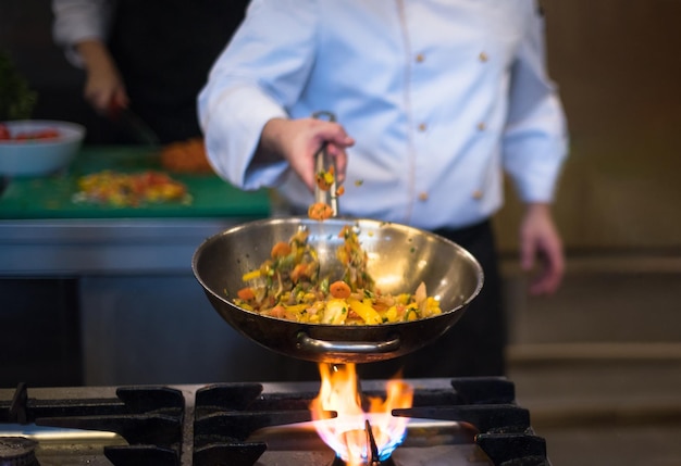 Macho joven chef voltear verduras en wok en cocina comercial