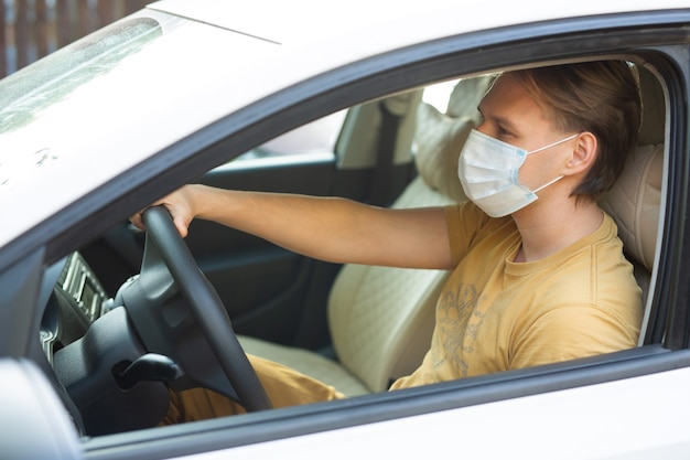 macho joven conduciendo un coche con una máscara médica