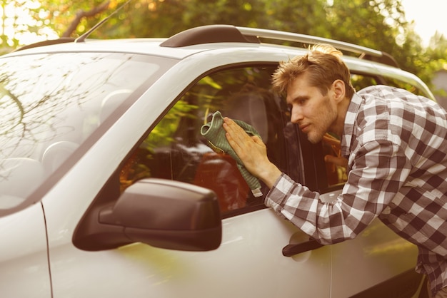 Macho joven conductor limpie su coche al aire libre en un día de verano