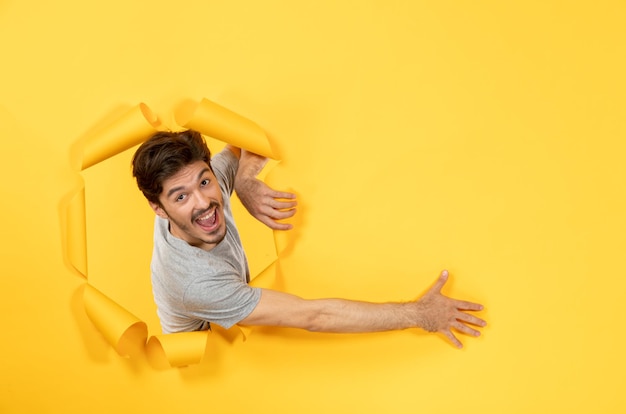 Macho joven mirando desde el fondo de papel amarillo rasgado facial venta chico interior