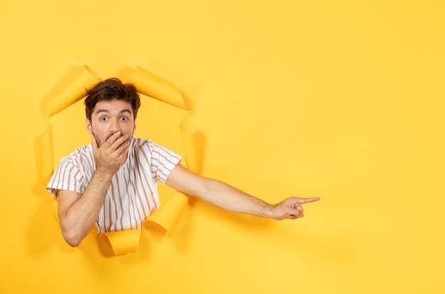 Macho joven mirando desde el fondo de papel amarillo rasgado tipo facial venta interior