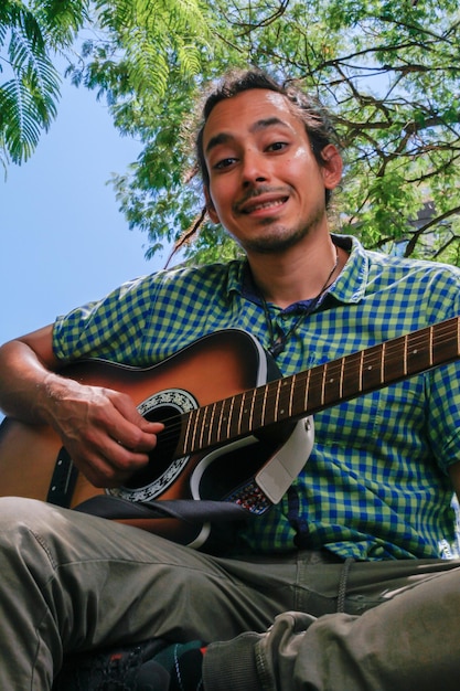 Macho joven con pelo rastas tocando una guitarra acústica marrón