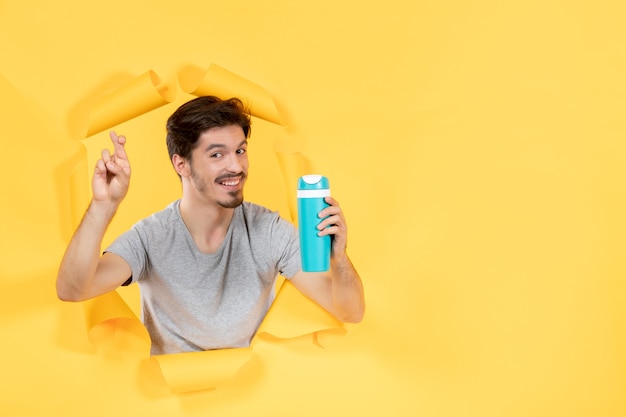 Macho joven sosteniendo una botella verde sobre fondo amarillo atleta deporte ajuste entrenamiento