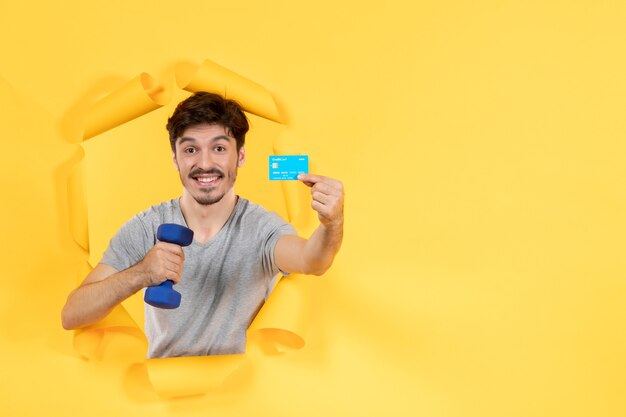 Macho joven con tarjeta de crédito y mancuernas sobre fondo amarillo dinero de entrenamiento ajuste atleta