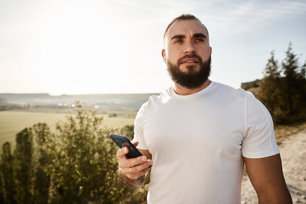 Macho joven con teléfono celular mientras da un paseo por el campo