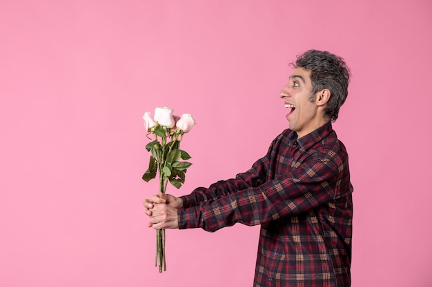 Macho joven de vista frontal dando hermosas rosas rosadas en la pared rosa