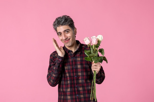 Macho joven de vista frontal con hermosas rosas rosadas en la pared rosa