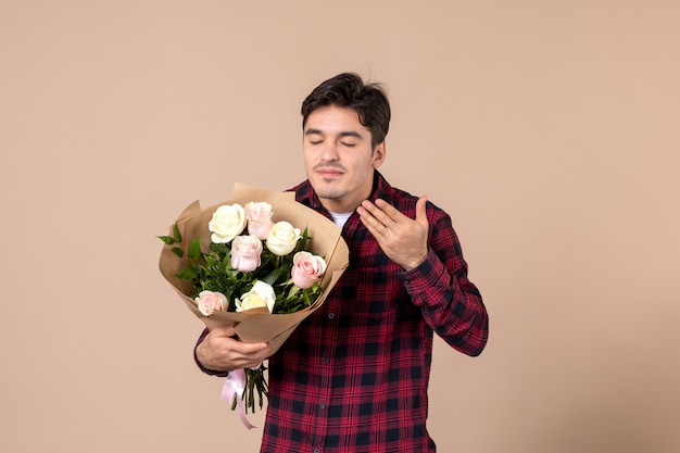 Macho joven de vista frontal sosteniendo hermosas flores en la pared marrón