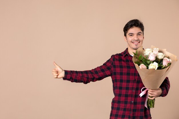 Macho joven de vista frontal sosteniendo hermosas flores en la pared marrón