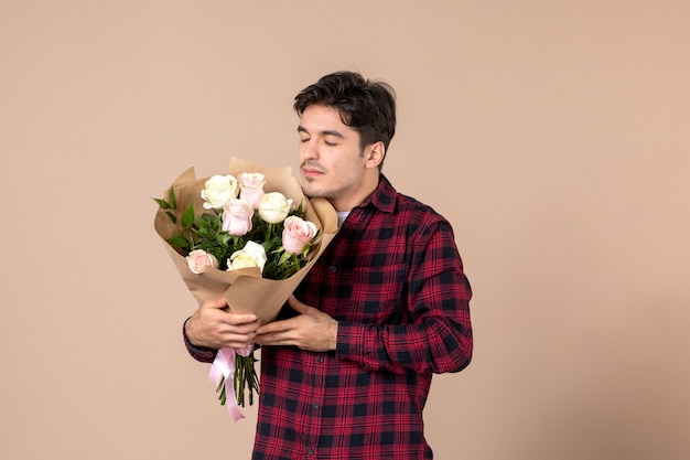 Macho joven de vista frontal sosteniendo hermosas flores en la pared marrón