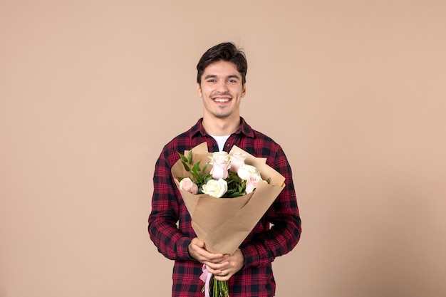 Foto macho joven de vista frontal sosteniendo hermosas flores en la pared marrón