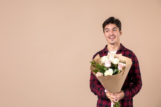 Macho joven de vista frontal sosteniendo hermosas flores en la pared marrón