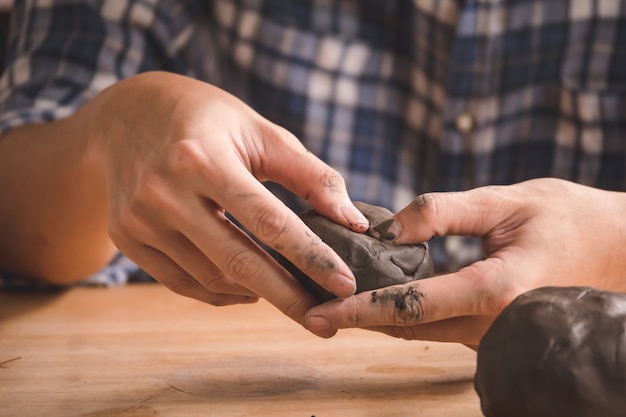 Macho mãos modelando um bloco de barro na mesa de madeira