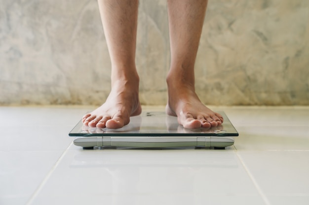 Foto macho na escala de peso no chão, conceito de dieta.