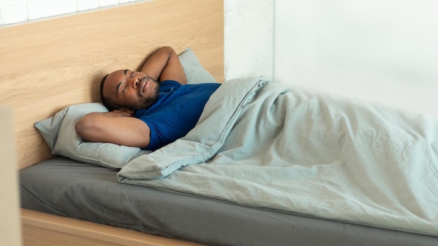 Macho negro dormindo na cama de mãos dadas atrás da cabeça interior