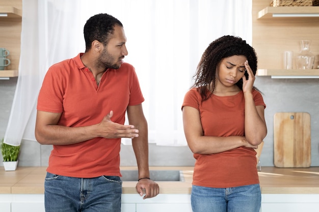 Macho negro milenar irritado repreendendo a esposa ofendida que sofre de pressão e estresse no interior da cozinha