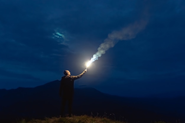 El macho con un palo de fuegos artificiales de pie sobre una montaña. Noche