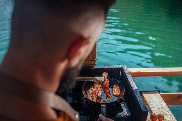 Macho preparando café da manhã ao ar livre próximo ao lago