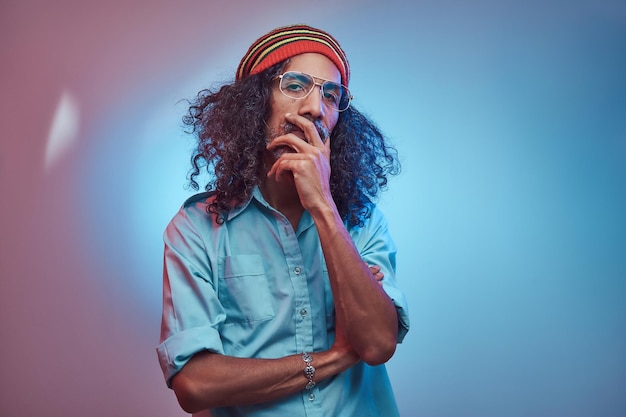 Macho rastafari africano pensativo vestindo uma camisa azul e gorro. Retrato de estúdio em um fundo azul.