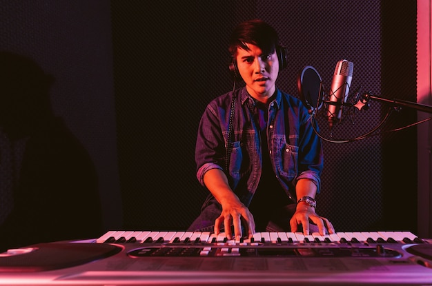 Macho tocando un teclado eléctrico mientras lleva puestos los auriculares Grabación de canciones