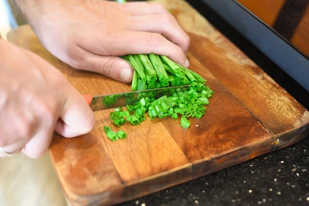 machos manos cortando cebolla verde en tablero de madera para cocinar ramen japonés