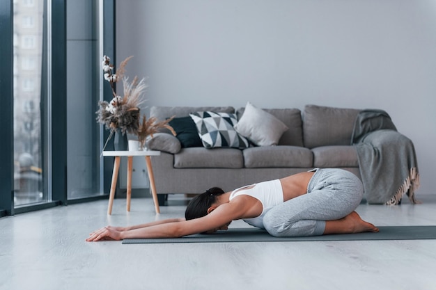 Macht flexible Übungen Junge Frau mit schlanker Körperform in Sportbekleidung hat Fitnesstag drinnen zu Hause