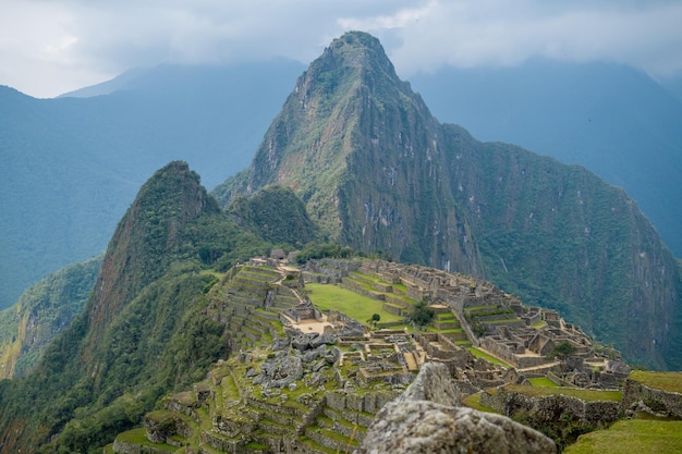 machu picchu al fondo con construcciones incas cercanas y cielo nublado al fondo