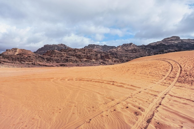 Maciços rochosos no deserto vermelho, marcas de veículos na areia, cenário típico em Wadi Rum, Jordânia