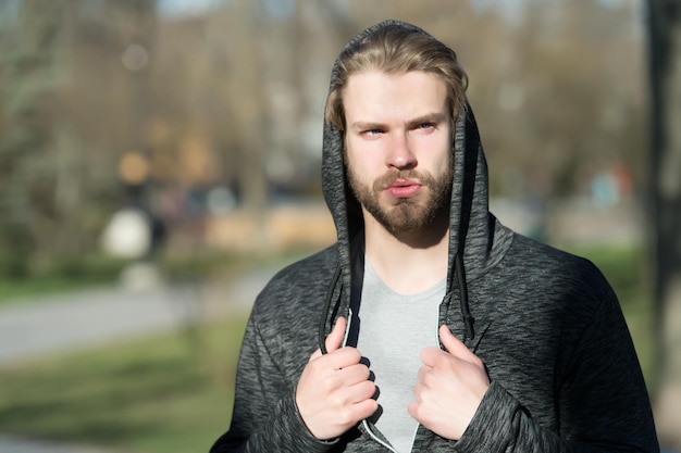 Maco mit unrasiertem Gesicht in Kapuze auf dem Kopf im Freien, Mode. Friseursalon, Friseursalon, Pflege. Mode, Stil, Schönheit.