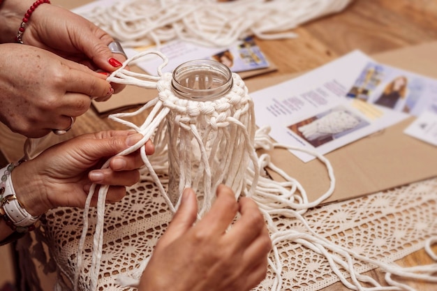 Macramé blanco Primer plano de las manos de dos ancianas atando nudos de macramé