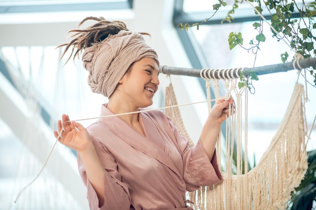 Macramé. Jovem mulher entrelaçando macramê em trajes caseiros