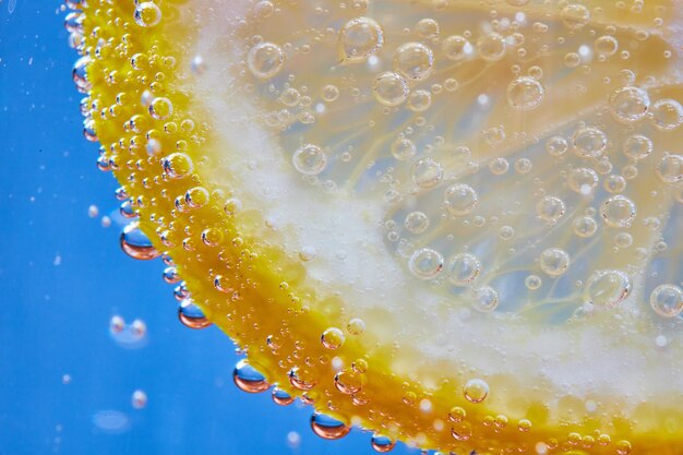 Foto macro de bolhas efervescentes na fatia de limão contra um fundo azul