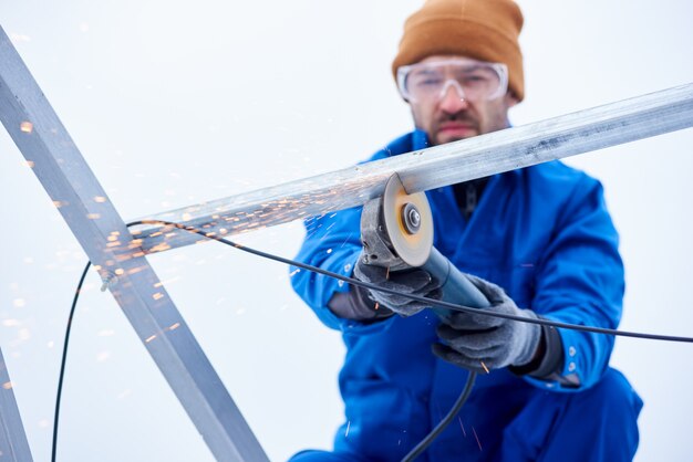 Macrofotografia de um homem búlgaro corta a moldura de um painel para instalar uma bateria solar. concentre-se na ferramenta búlgara