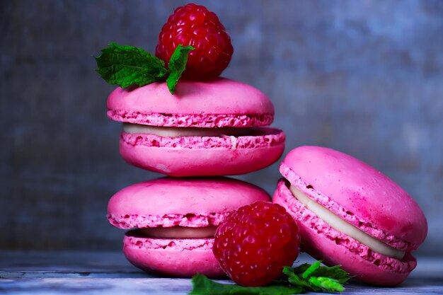 Macrones de frambuesa rosa fresca con relleno de helado y frambuesas frescas. Fondo gris borroso.