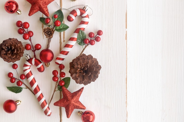 Madeira branca com pinhas ou cone de coníferas, bolas vermelhas de azevinho, estrela de glitter, pirulito e bugiganga no conceito de Natal. Fundo bonito da prancha na vista superior plana colocar cópia espaço para papel de parede de Natal