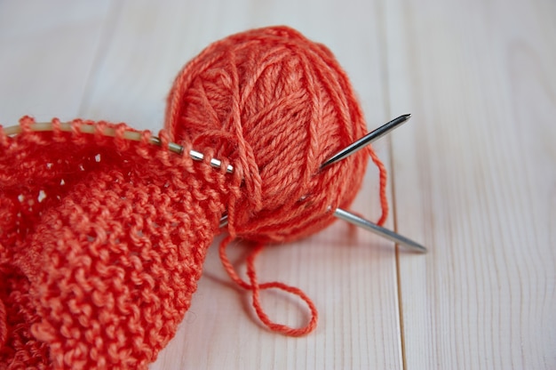 Madeja de hilo rojo de lana, con agujas para tejer a mano sobre una mesa de madera