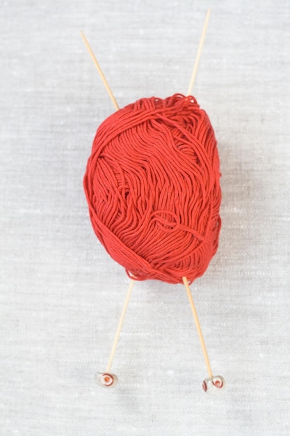 una madeja roja de hilo y dos agujas de tejer de madera sobre un fondo de tela gris