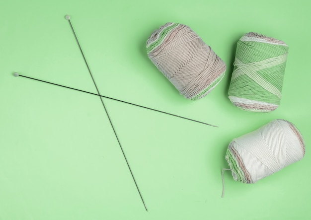 Madejas de hilos de lana de color pastel con agujas de tejer sobre fondo verde. Pasatiempos de las amas de casa