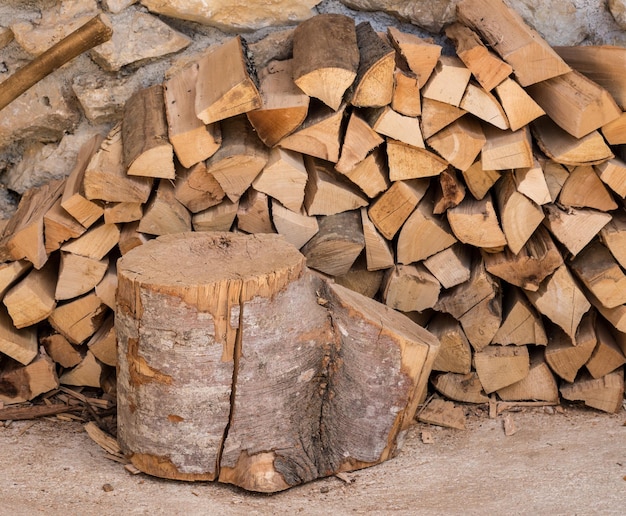 Madera cortada y hacha apiladas contra la pared de piedra de una granja rústica