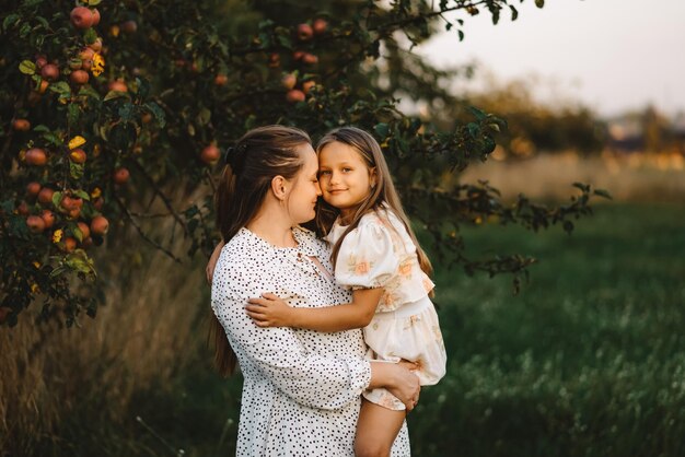 Una madre abraza a su hija en un huerto de manzanos al atardecer